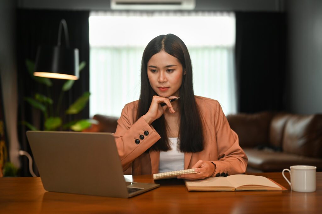 Thoughtful asian businesswoman watching online webinar and working online.